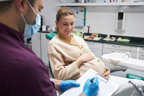 Dentist doctor prescribing a treatment to a pregnant woman smiling while sitting on dental chair