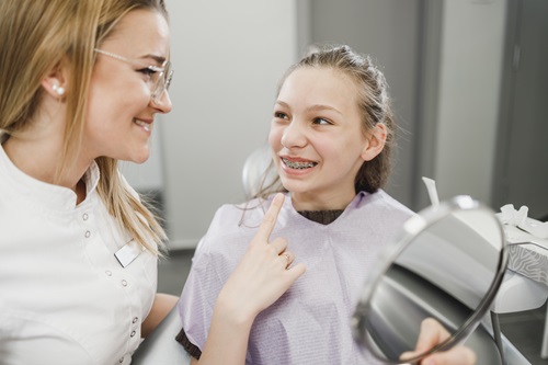 A happy teenager girl looking her teeth in a mirror after dental procedure at dentist's office.