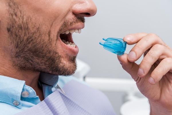 cropped view of bearded man with opened mouth holding snoring mouthguard