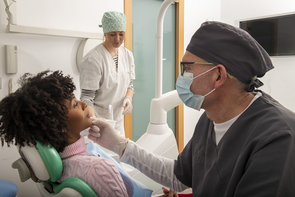 Dentist wearing mask and gloves examining patient's teeth for crown restoration.