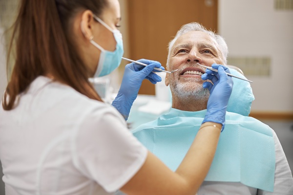 Skillful young female dentist holding dental tools while examining an elderly man