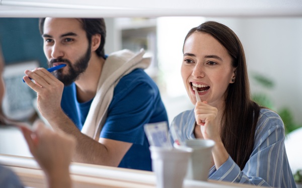 Portrait of young couple brushing teeth in front of mirror indoors at home.